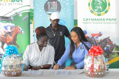 Aswanda Stoddart, Assistant Vice President of Administration at Supreme Ventures Racing and Entertainment Limited (SVREL) (left), joyfully participates in a signing ceremony with Ayawna Morgan, Category Manager Beverage at ICOOL (right). The occasion marks the official agreement between Caymanas Park and ICOOL Water and Drinks on Tuesday at Caymanas Park. Jockey Phillip Parchment (in the background) witnesses the significant event with enthusiasm.