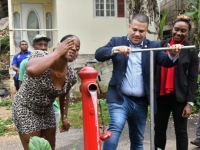 Water pours from a fire hydrant turned on by Minister Without Portfolio in the Ministry of Economic Growth and Job Creation, Matthew Samuda (centre), while resident of Sterling Castle Heights, St Andrew, Suzanne Thompson (left), splashes some on her face. The occasion was the commissioning into service of a recently completed pipeline replacement project and upgrading works in the community on June 8. Looking on at right is Member of Parliament for West Rural St Andrew, Juliet Cuthbert- Flynn.